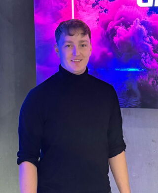 Bild von Unilumin Sales Manager „Robin Pollinger“. Junger Mann mit braunem, kurzen Haar, gekleidet mit einem schwarzen Rollkragenpullover.